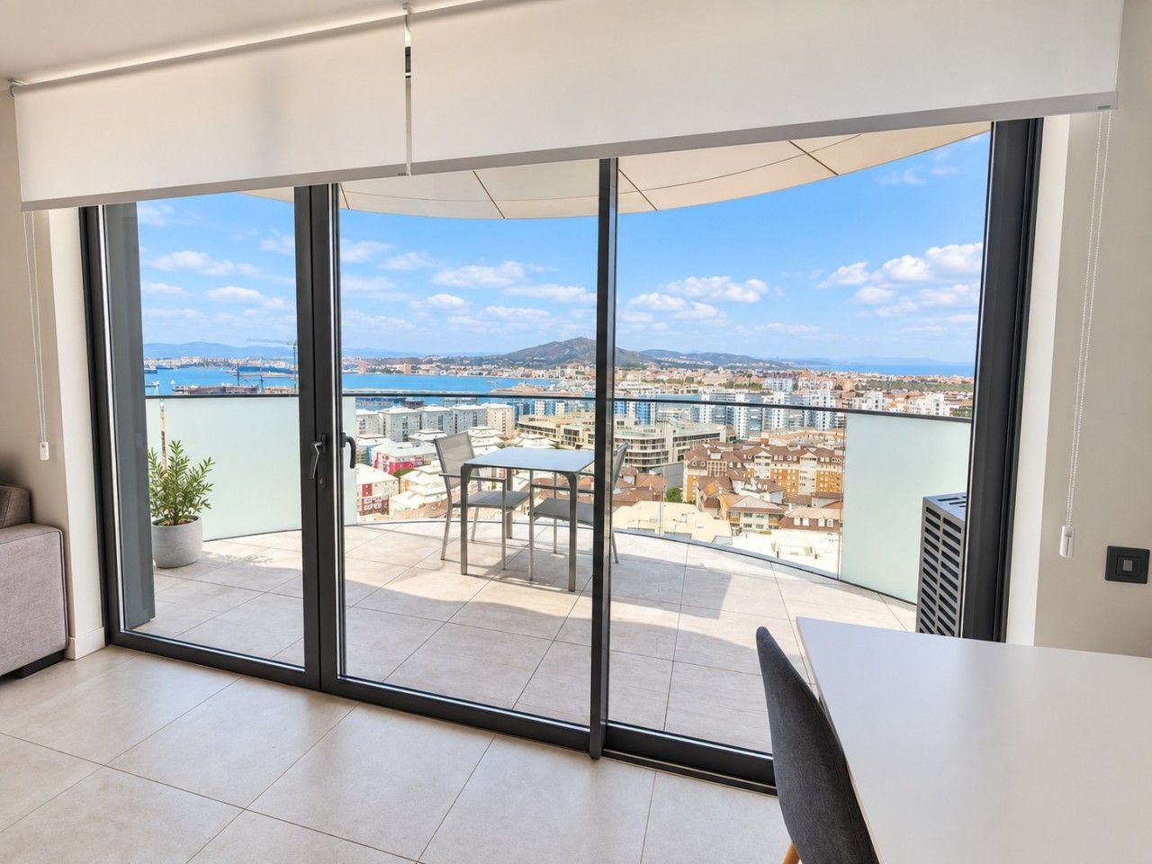 Un apartamento moderno con un gran ventanal corredera que da a un balcón con vistas a la ciudad.