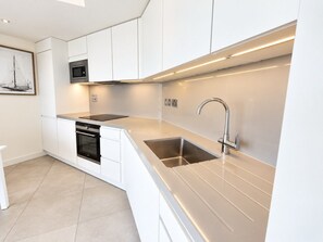 Una cuina moderna amb armaris blancs, un vàter d'acer inoxidable i un forn encastrat.