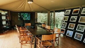 Une pièce aménagée comme une tente, avec une table et des chaises en bois, un téléviseur et un mur recouvert de photographies d’animaux sauvages encadrées.