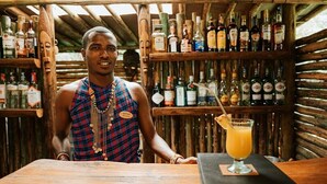 Un espace bar avec des étagères en bois remplies de différentes bouteilles, un comptoir de bar et un verre de jus d’orange avec une paille.