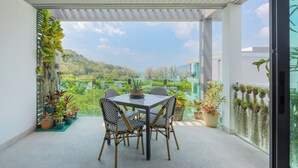 Ein Balkon mit Tisch und Stühlen, umgeben von Blumentöpfen und Blick auf eine üppige Landschaft.