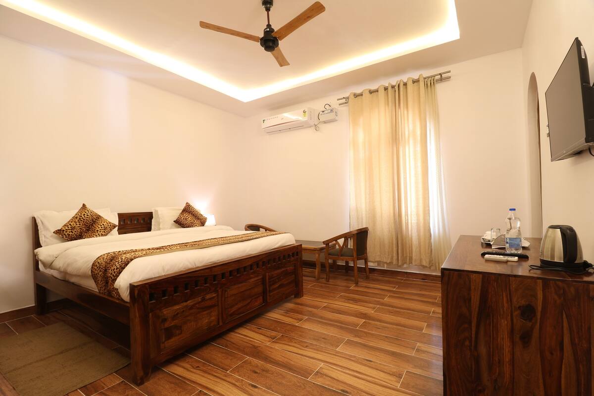A hotel room with a wooden bed, a desk, a ceiling fan, an air conditioning unit, and a TV mounted on the wall.