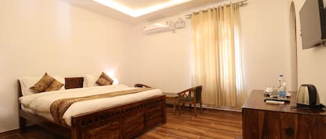 Ein Hotelzimmer mit einem hölzernen Bett, einem Schreibtisch, einem Deckenventilator, einer Klimaanlage und einem an der Wand befestigten Fernseher.