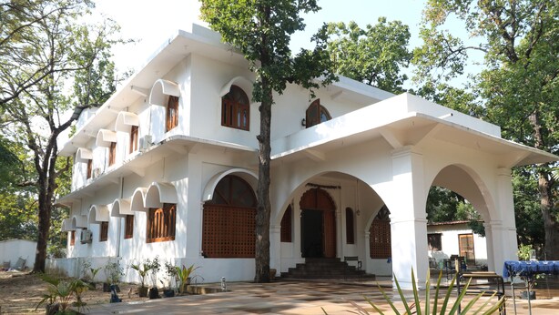 A white building with multiple arches and balconies, surrounded by trees and potted plants.