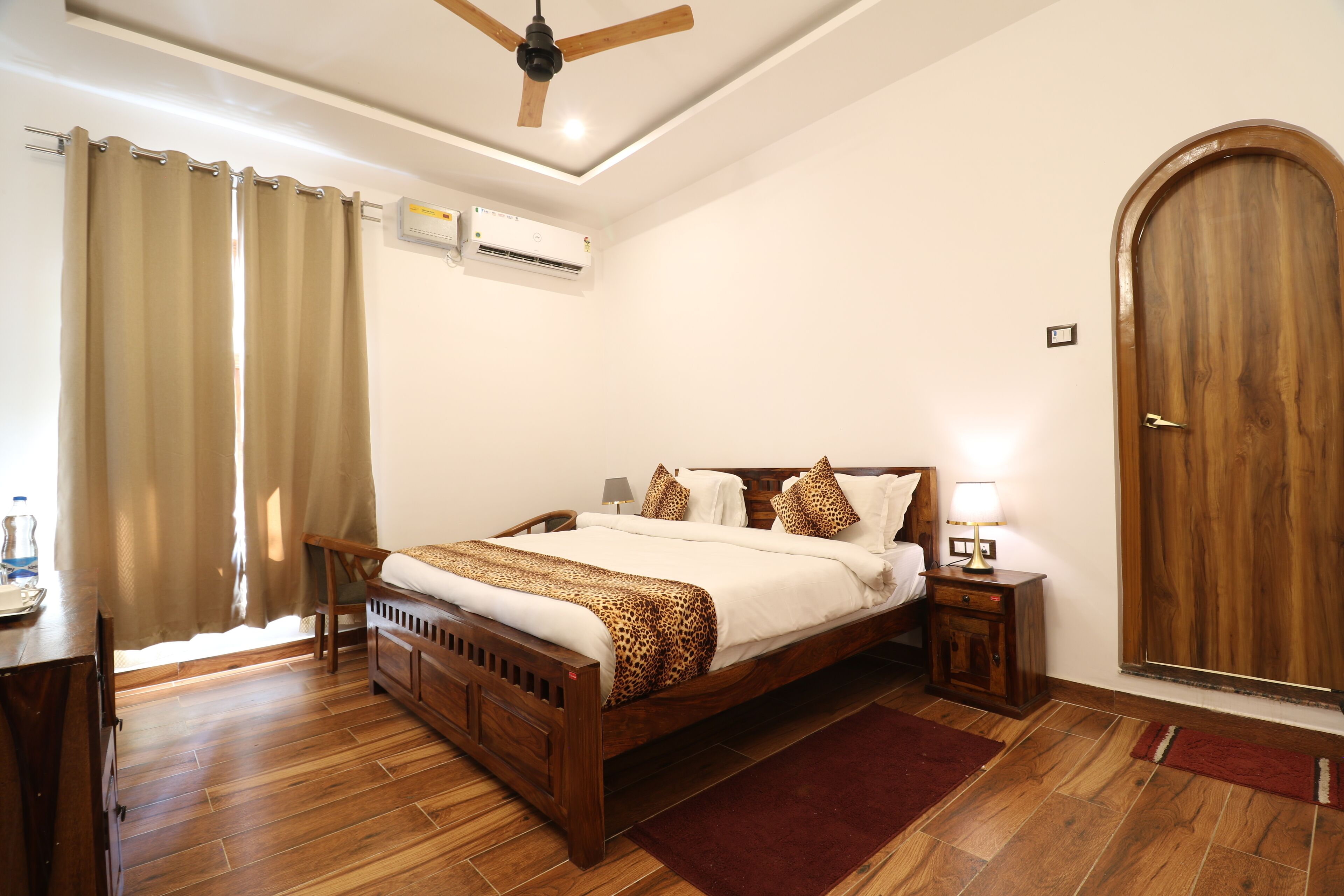 Un dormitorio con una cama de madera, ventilador de techo, unidad de aire acondicionado, puerta de madera y un escritorio con silla.