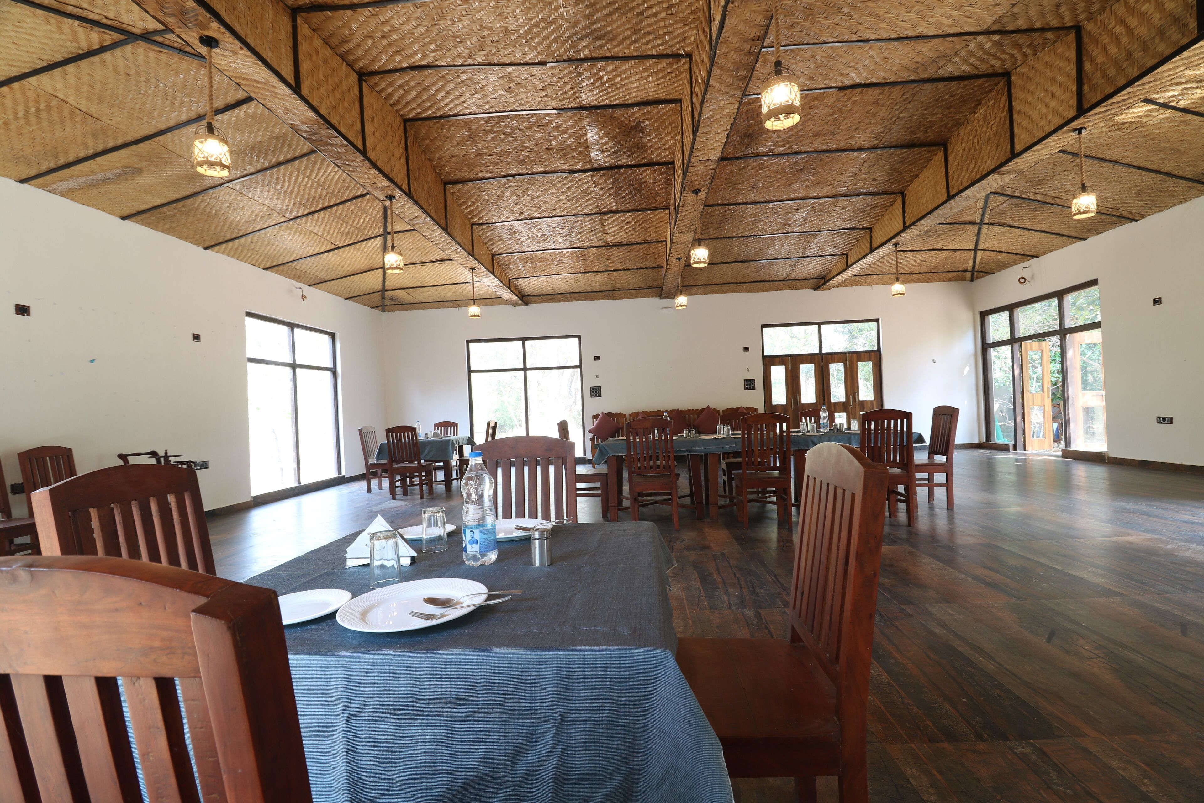 A spacious dining area with high ceilings and natural light. Tables are set with plates and cutlery.
