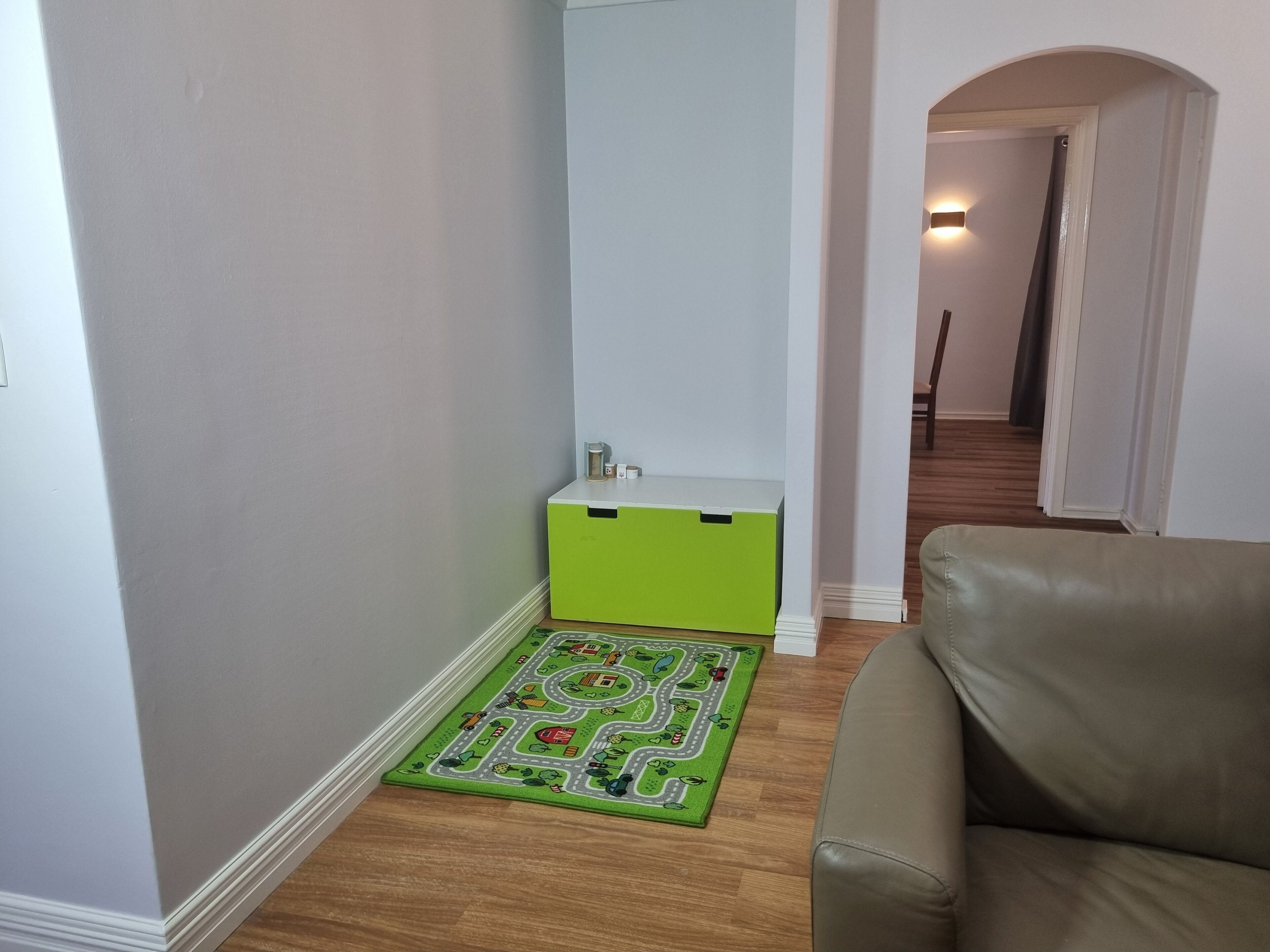 Ein Flur mit einem grünen Schrank, einem grün-weißen Teppich und einem Ledersofa.