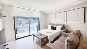 Ein modernes Schlafzimmer mit Bett, einer Couch, einem Fernseher und einem großen Fenster mit Blick auf die Stadt.