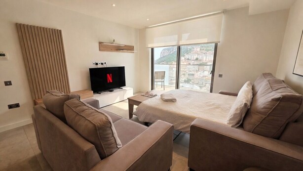 Ein modernes Hotelzimmer mit Bett, Sofa, Fernseher und einem Balkon mit Blick auf die Stadt.