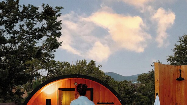 A person entering a wooden sauna with a bench inside, set against a backdrop of trees and mountains. - Lux Casa HotTub + Sauna w/ Mtn Views, DT 10mins (Santa Fe)
