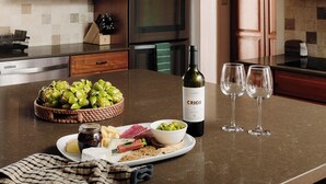 A kitchen counter with a bottle of wine, two glasses, a plate with cheese, olives, and a basket of artichokes. - Lux Casa HotTub + Sauna w/ Mtn Views, DT 10mins (Santa Fe)