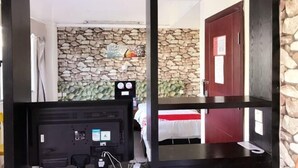 A room with a stone wall, a bed with a red headboard, a desk with a computer, and a door with a red handle. - Sanya Mingjing Express Hotel (Sanya)