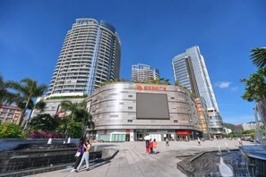 A modern building with a curved facade, a large central entrance, and a surrounding plaza with palm trees and a fountain. - Sanya Mingjing Express Hotel (Sanya)