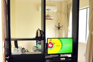 A room with a television, a desk with a lamp, a window with curtains, and a wall-mounted air conditioning unit. - Sanya Mingjing Express Hotel (Sanya)