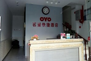 Een receptiebalie met een klok, een bord met 'OYO' en Chinese karakters, en een trap die naar een verdieping leidt.