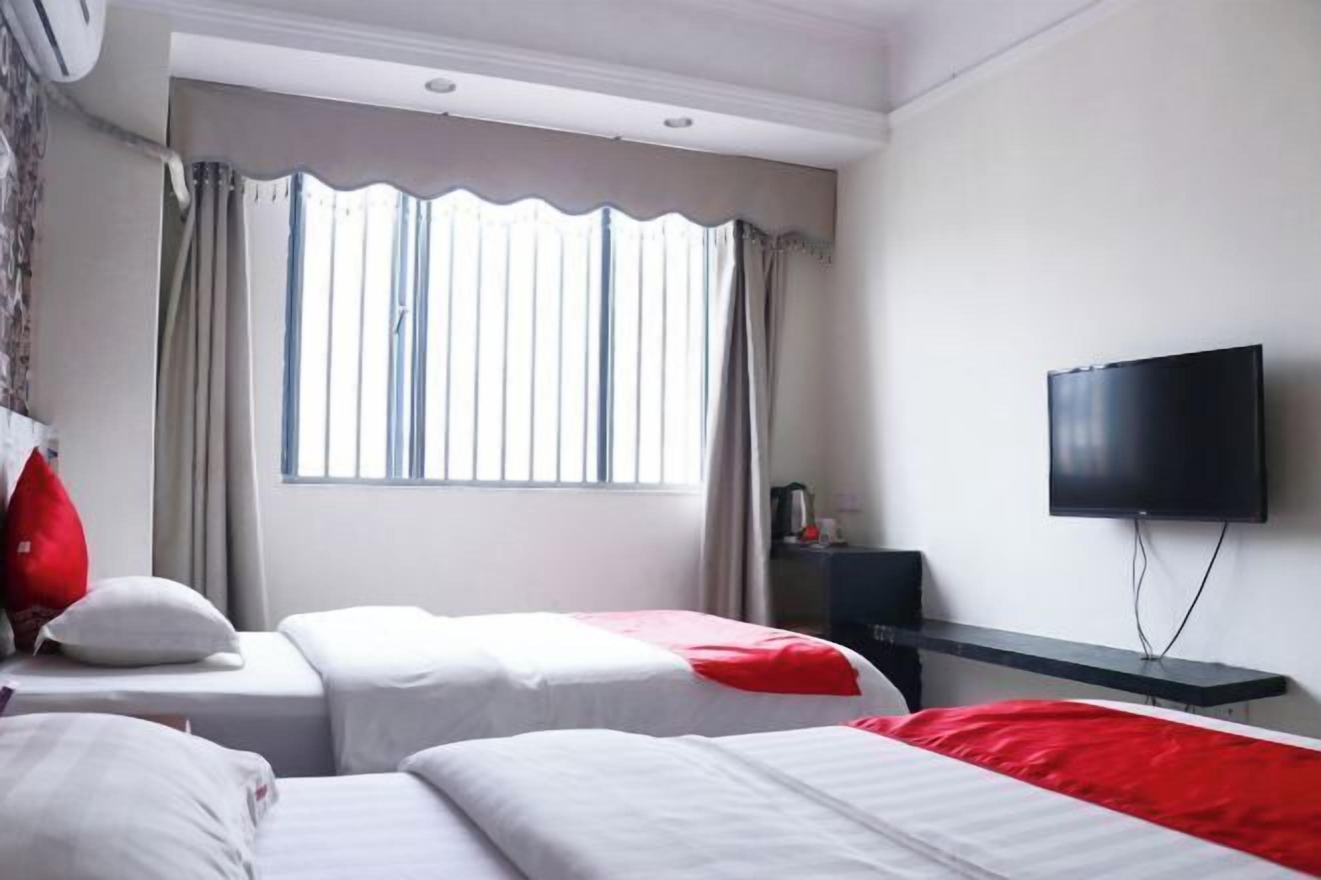 Una habitación de hotel con dos camas, televisión, ventana con cortinas y una pequeña mesa con lámpara.