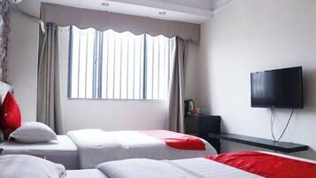 Una habitación de hotel con dos camas, televisión, ventana con cortinas y una pequeña mesa con lámpara.