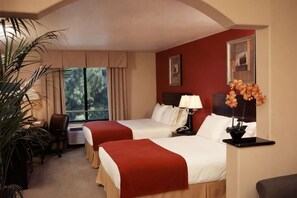Een hotelkamer met twee bedden, een bureau, een stoel, een raam met gordijnen en een potplant.