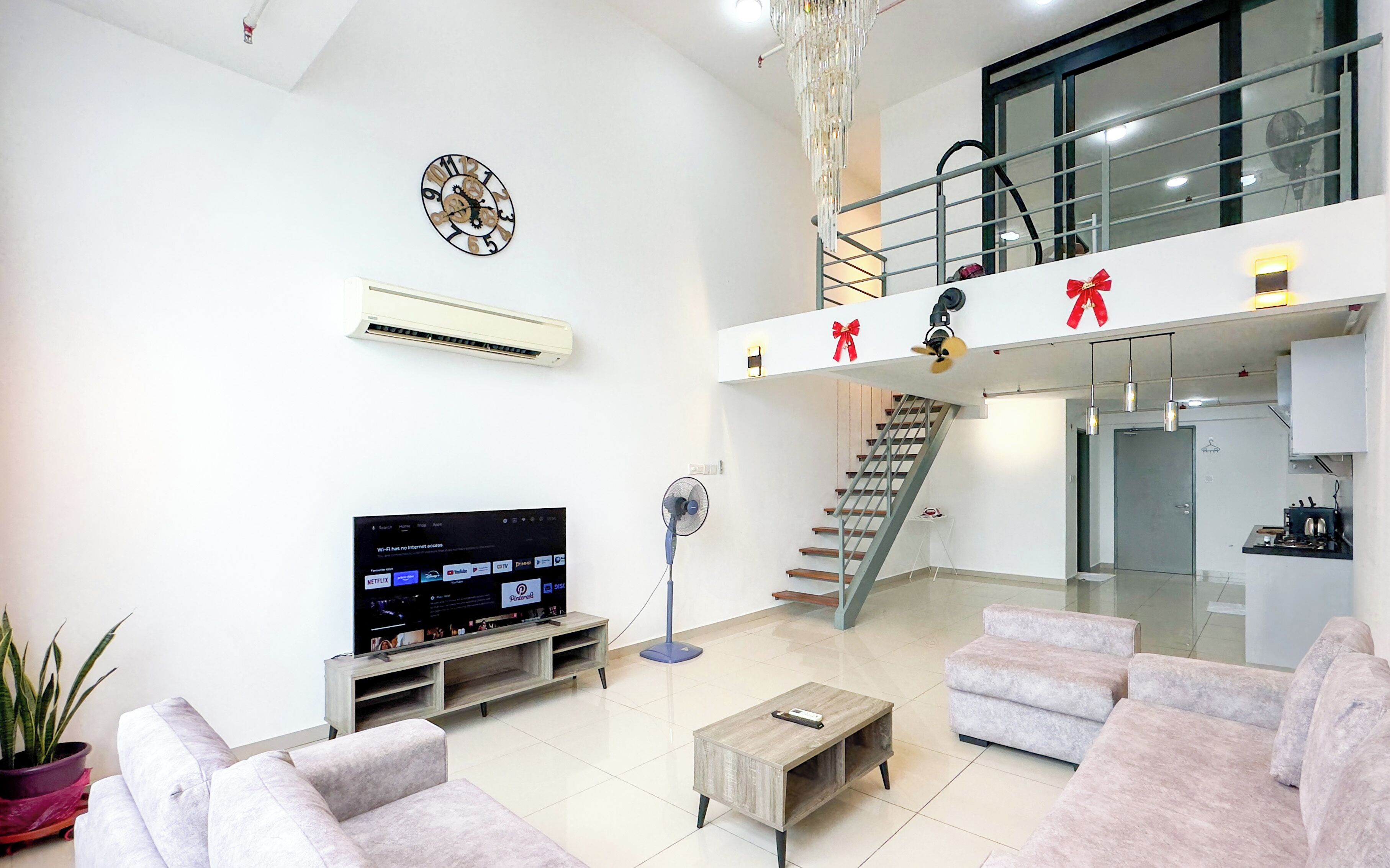 A modern living room with a flat-screen TV, a clock, a fan, and a staircase leading to an upper level.