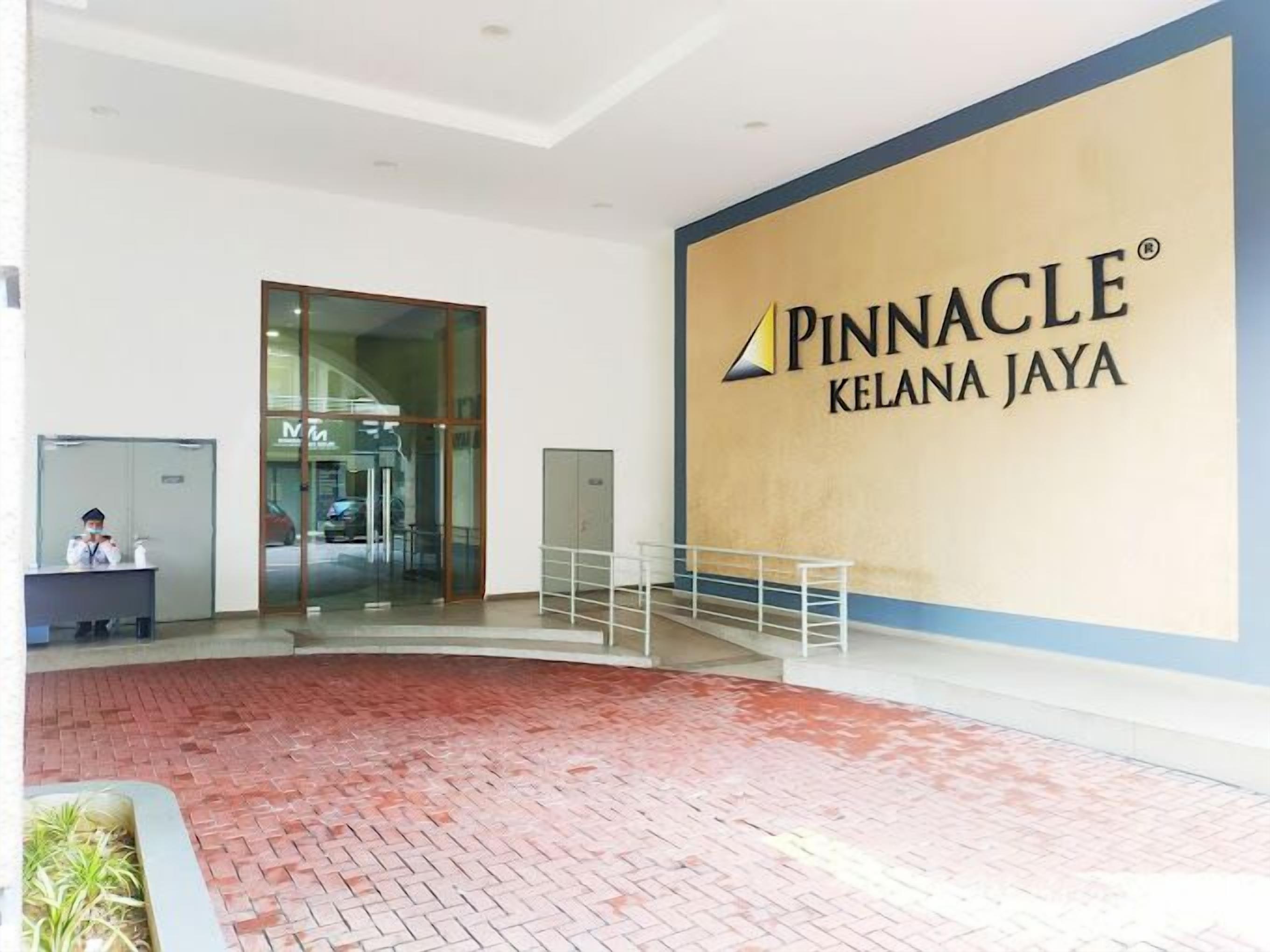 A Pinnacle Kelana Jaya hotel lobby with a reception desk, glass doors, and a large sign.
