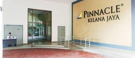 A Pinnacle Kelana Jaya hotel lobby with a reception desk, glass doors, and a large sign.