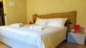 A neatly made bed with white linens and rolled towels, a wooden headboard, a bedside table with a red vase, and a nightstand with a red object on it. - Il Carro Rooms (Monza)