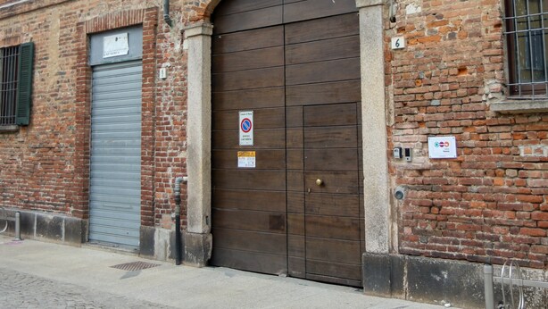 A brick building with a large wooden door, a garage door, and a small window with shutters. - Il Carro Rooms (Monza)