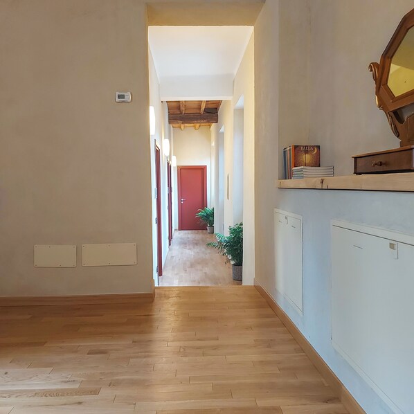 A hallway with wooden flooring, a red door at the end, and a radiator on the right wall.
