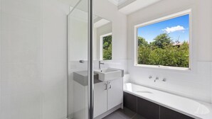 A modern bathroom with a glass shower enclosure, a sink, and a large window offering a view of greenery. - Warm Country Side Home (Buxton)