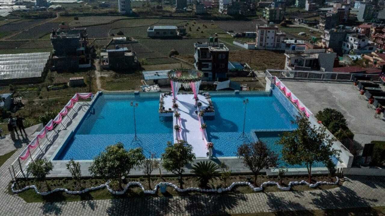 A rectangular swimming pool with a central platform, surrounded by a paved deck and a low wall.
