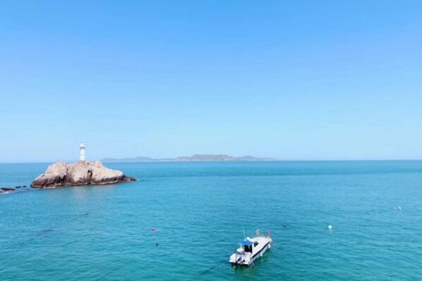 A lighthouse on a rocky island with calm sea and a boat in the foreground. - Dahai Zhizi Inn (Zhoushan)