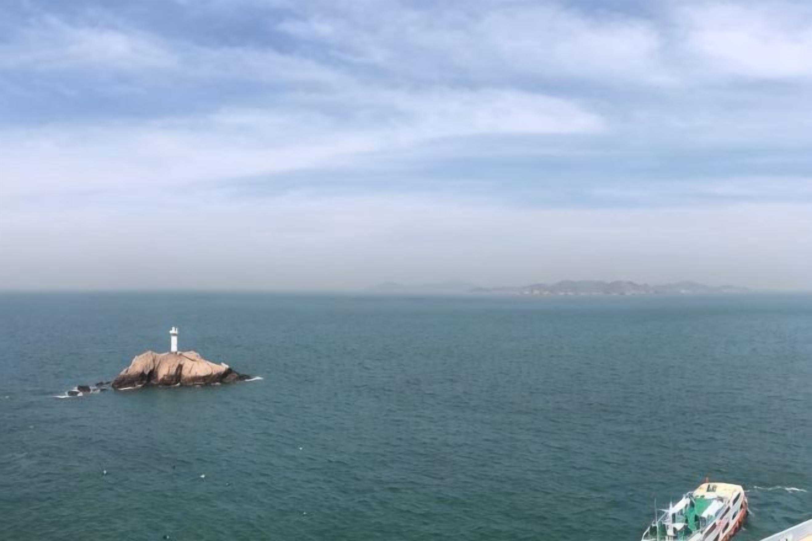 A lighthouse on a small island in the ocean with a boat in the foreground.