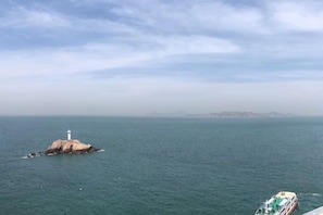 A lighthouse on a small island in the ocean with a boat in the foreground. - Dahai Zhizi Inn (Zhoushan)