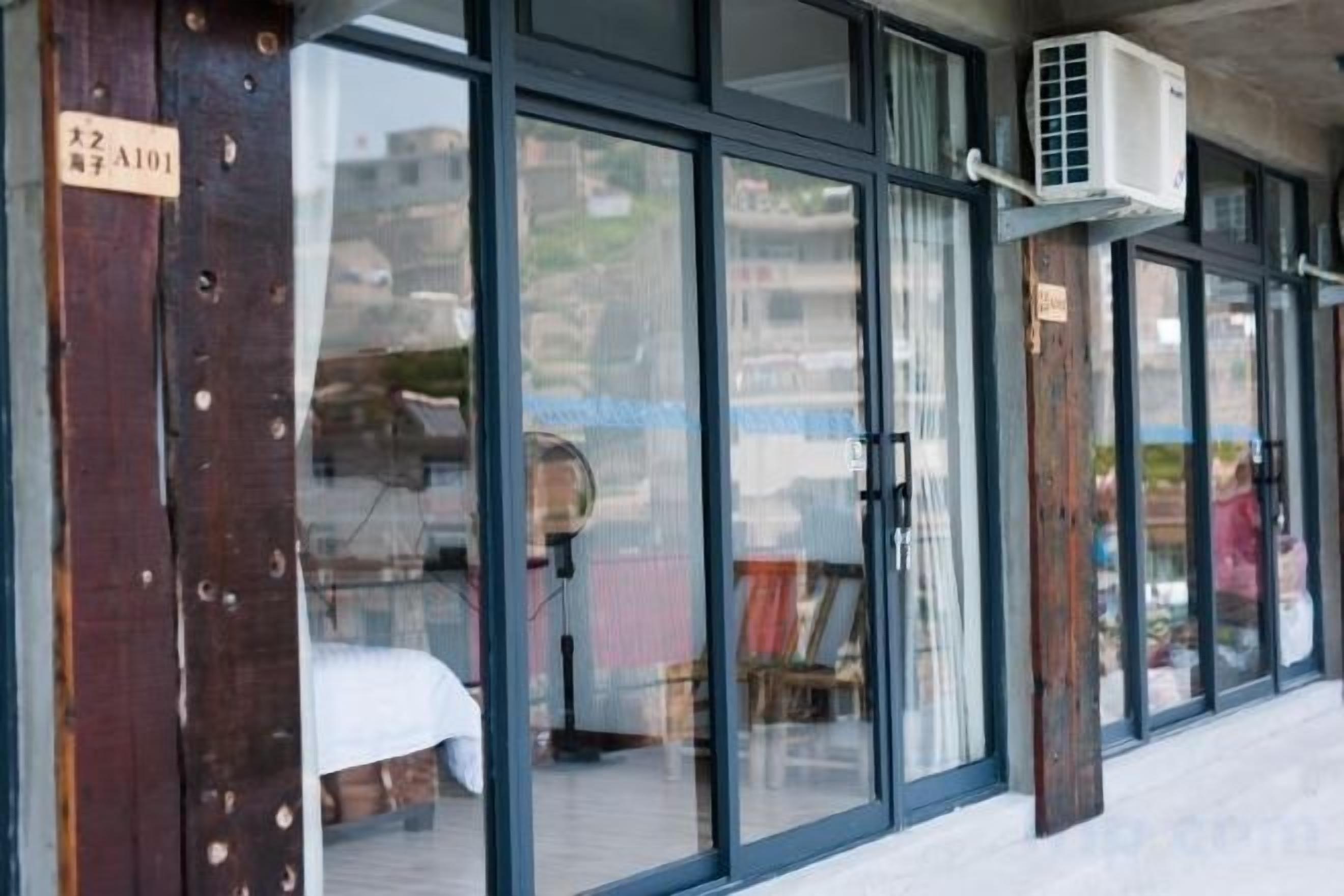 A hotel entrance with large glass doors, a wooden pillar with a sign, and an air conditioning unit mounted on the wall.