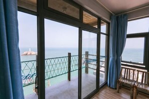 A room with large windows, a balcony with a view of the sea, and a wooden bench.