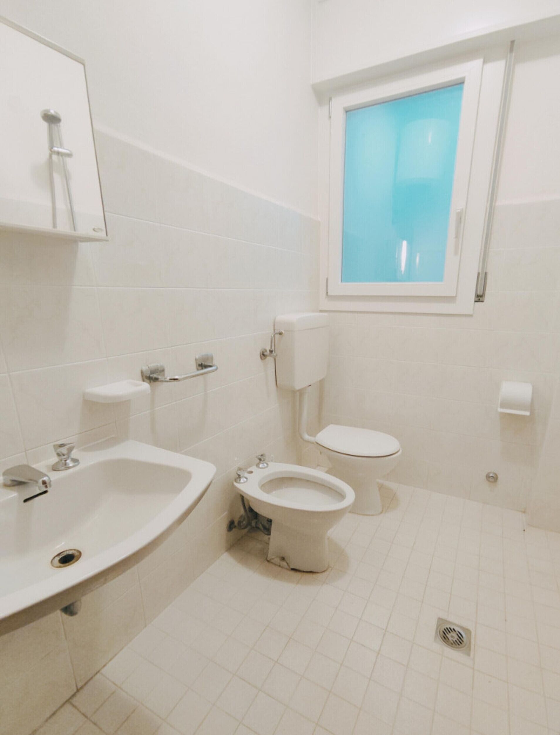 Ein kleines, sauberes Badezimmer mit Waschbecken, Toilette und Fenster.