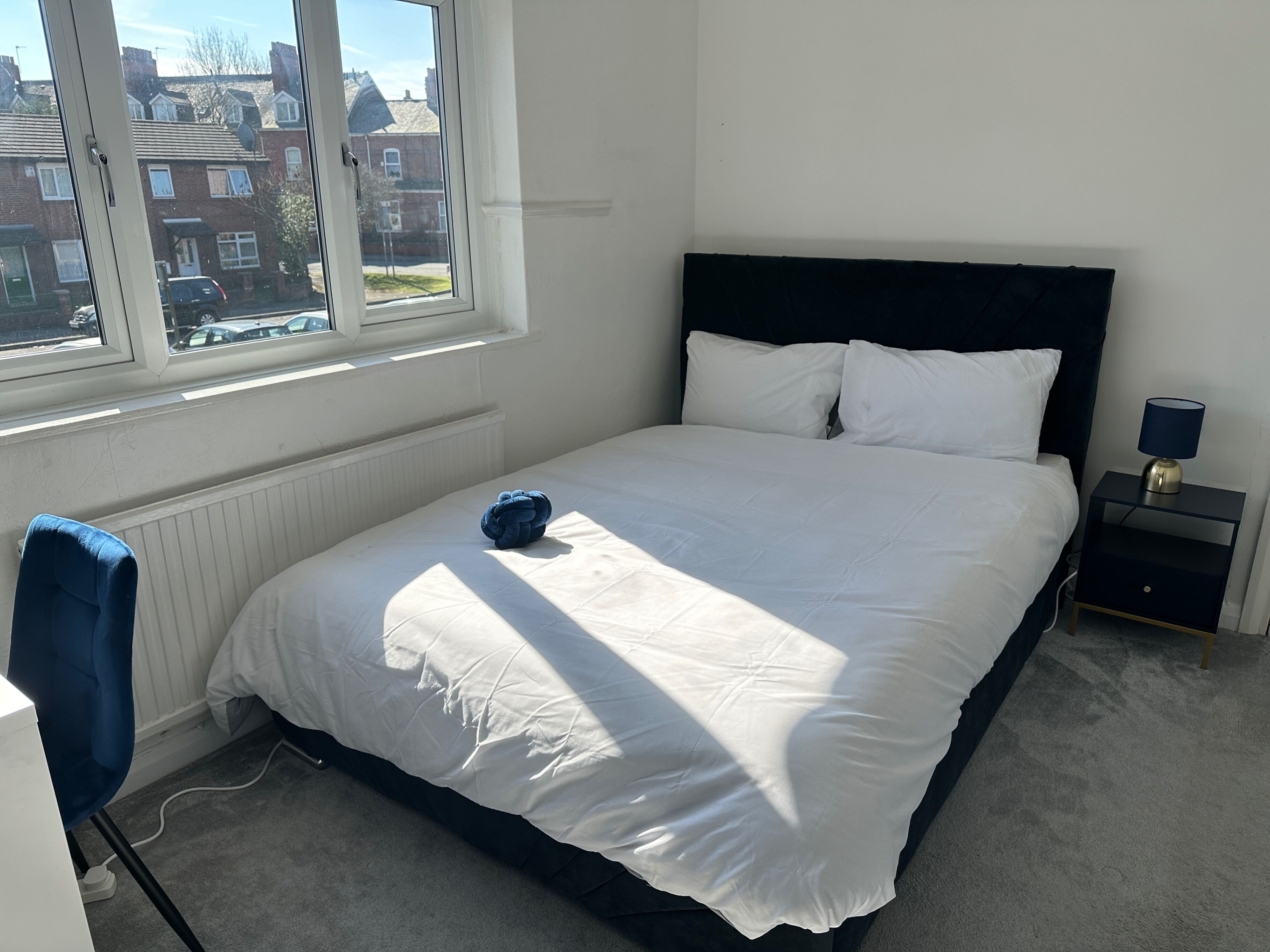 A bedroom with a large bed, a window, a bedside table, and a chair.