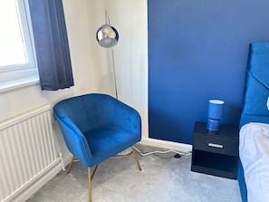 A room with a blue chair, a bedside table with a lamp, and a window with curtains. - Up to 40 Percent Off Old Trafford 3 Bed (Manchester)