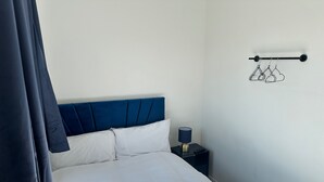 A neatly made bed with white linens, a blue headboard, and a bedside table with a lamp and remote control.