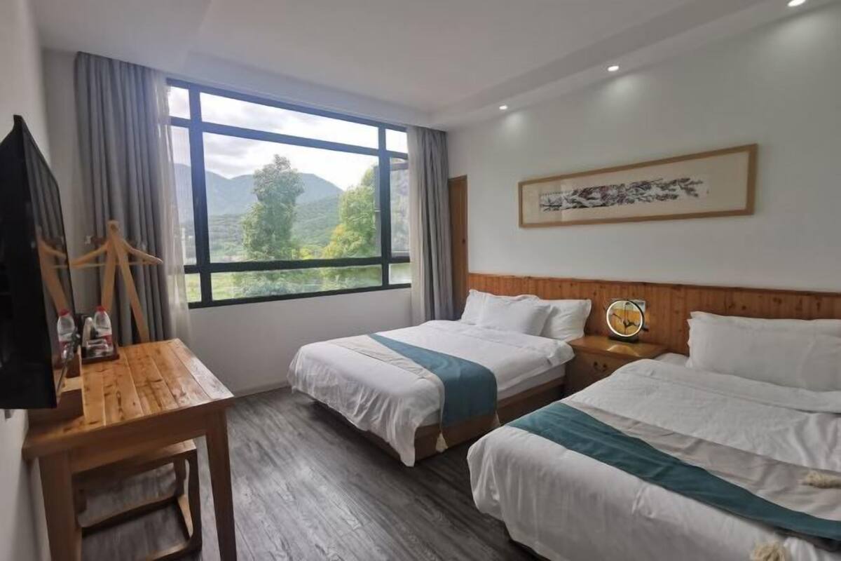 Habitación de hotel con dos camas, un escritorio de madera, televisor y un amplio ventanal con vistas a la montaña.