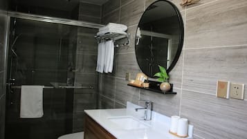 Un baño con cabina de ducha de vidrio, un lavabo blanco, un espejo y un perchero para toallas.
