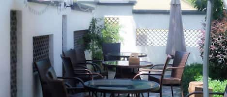 Une terrasse extérieure avec des tables et des chaises rondes, une plante en pot et un parasol blanc.