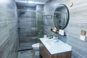 A modern bathroom with a glass shower enclosure, a toilet, a sink with a mirror, and a shelf with toiletries. - Taohua Island Taoyuanli Homestay (Zhoushan)