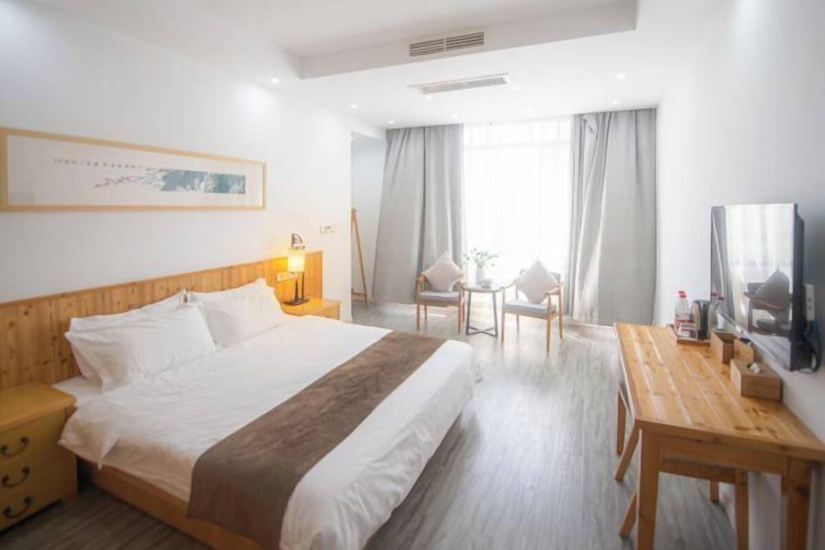 Una habitación de hotel con cama, escritorio, silla, una mesita y ventana con cortinas.