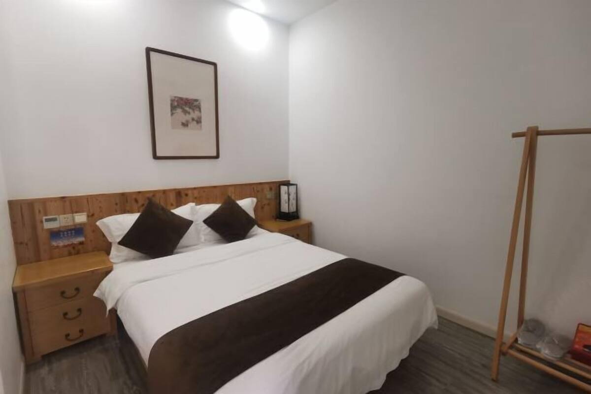 Una cama bien hecha con cabecera de madera, una mesita de noche con cajones, un cuadro en la pared y un tocador de madera con espejo.