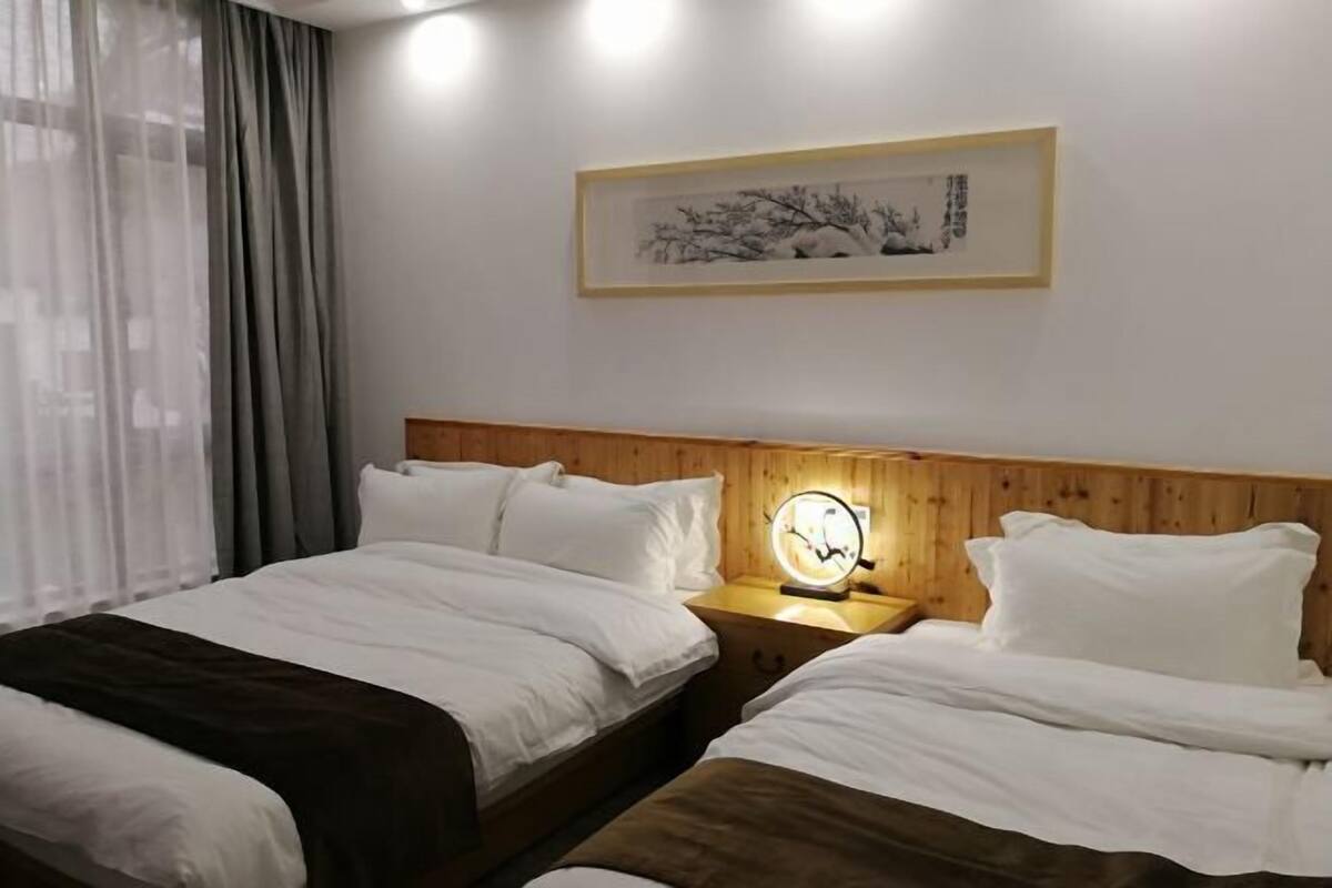 Habitación de hotel con dos camas, cabeceros de madera, una mesita de noche con lámpara y una obra de arte enmarcada en la pared.