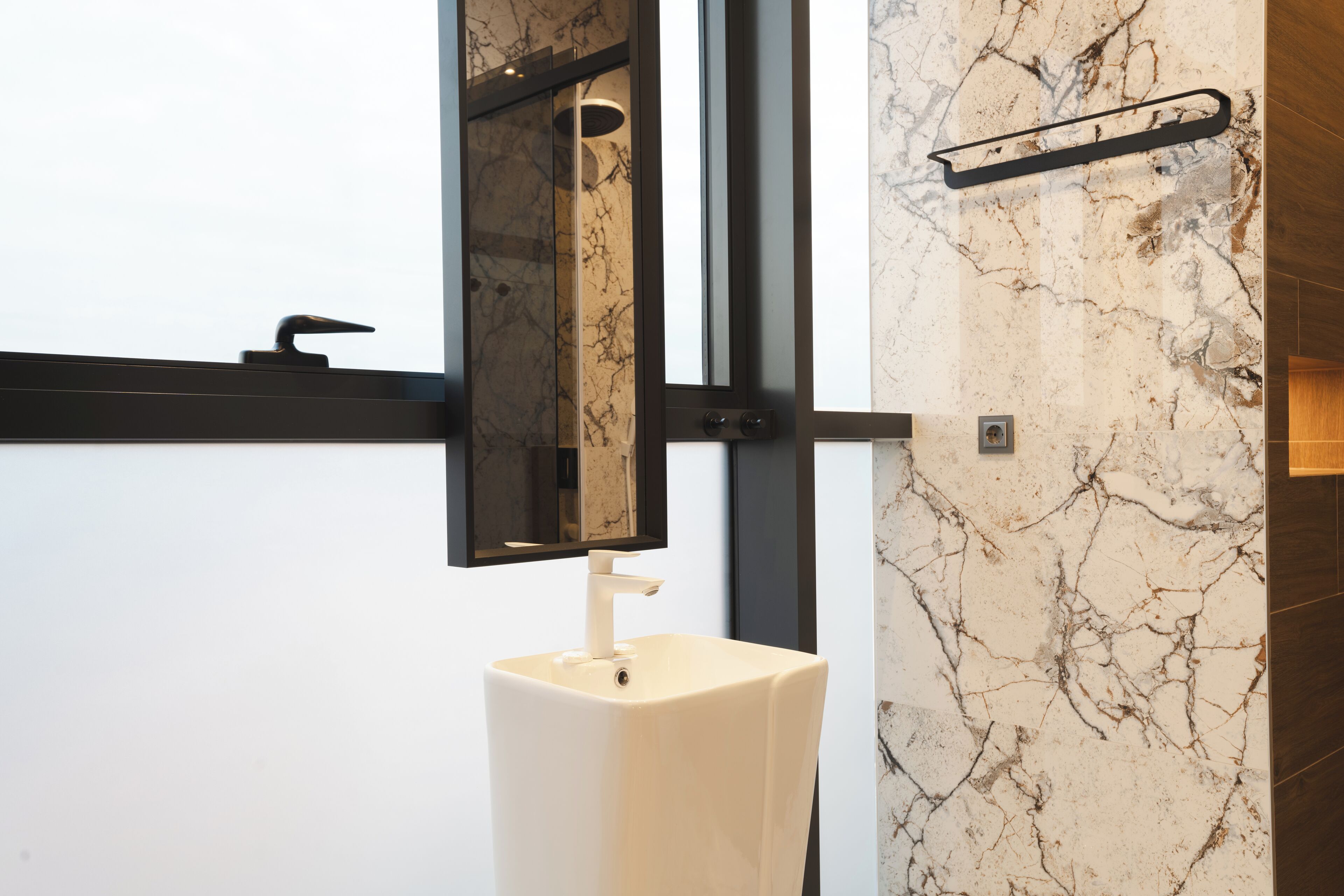 A bathroom with a white pedestal sink, a mirror, and a marble wall.