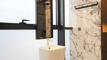 A bathroom with a white pedestal sink, a mirror, and a marble wall.