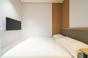 Ein modernes Schlafzimmer mit Bett, Holz-Kopfteil, montiertem Fernseher und kleinem Holztisch.