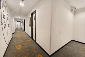Pasillo de hotel con puertas a ambos lados, una alfombra estampada y una pared lisa con un accesorio de iluminación.